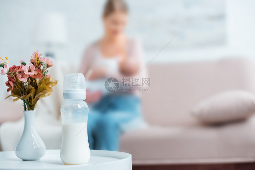 近距离观看婴儿瓶装牛奶花瓶中的鲜花和母亲在家后图片