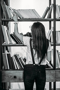 年轻女站在书架旁选择书籍的黑人和白人图片