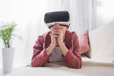 女孩躺在沙发上在家里用虚拟现实耳机图片