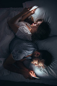 年轻夫妇背靠躺在床上晚上用图片