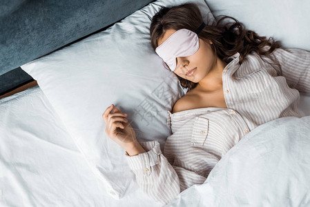 年轻的黑发女人睡在床上的眼罩图片