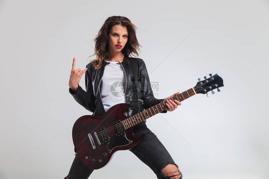 酷的女吉他手在灰色背景上做岩图片