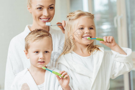 美丽的幸福母亲和穿浴袍的小孩一起刷牙图片