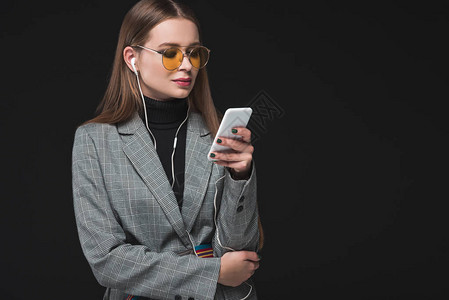 穿着灰色夹克和黄色眼镜的漂亮女人听着音乐用智能手机图片