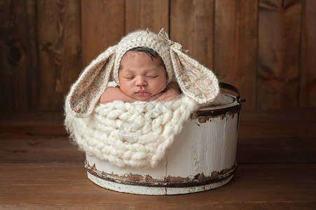 一个三周大的新生女婴睡在一个的小木桶里她戴着一顶奶油色的帽在木图片
