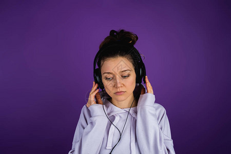 严肃的女孩在耳机里听悲伤的音乐穿着紫色图片
