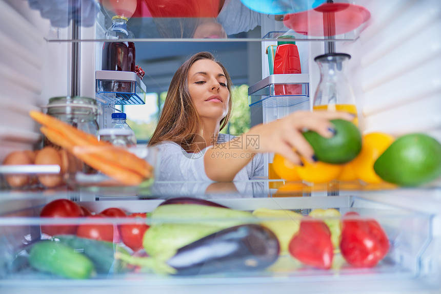 站在开着的冰箱前吃鳄梨的女人满图片