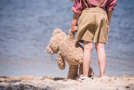 小女孩站在岸边时拿着泰迪熊的图片