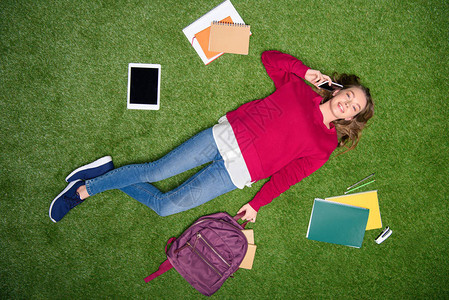 年轻学生在休息绿草坪的同时用智能手图片