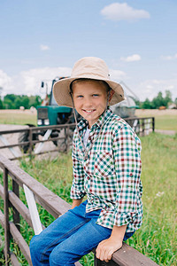 穿着巴拿马帽子的快乐男孩坐在栅栏上对农图片