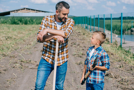 父亲和儿子拿着铲子在农场上图片