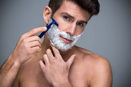 英俊的男人刮胡子在灰色的背景图片