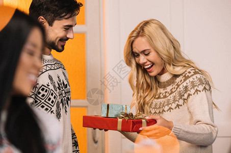 快乐的女人看着礼物与微笑的男朋友手牵在圣诞节在家附近图片