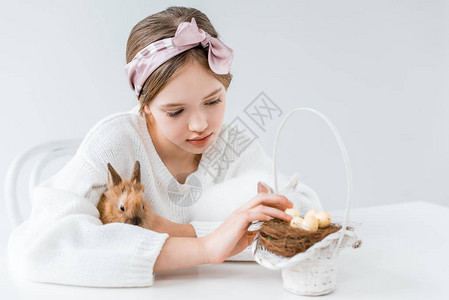 可爱的小女孩抱小兔子看着篮子窝里图片