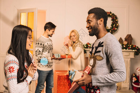 多种族多裔青年夫妇在家中庆祝期间交换圣诞礼物的图片