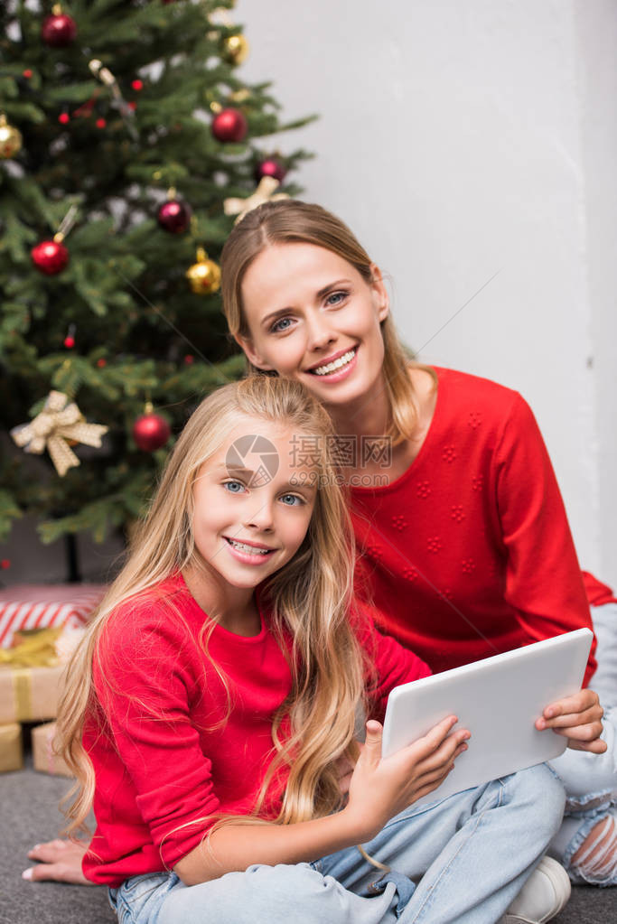 母亲和女儿微笑在圣诞节树上使用带有礼品图片