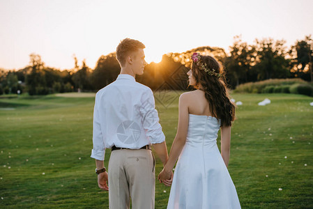年轻结婚夫妇握着手在日落图片