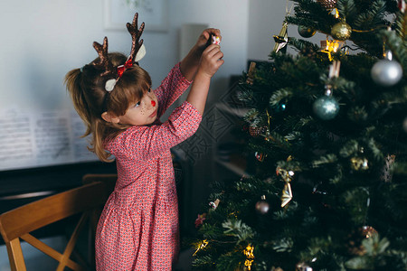 可爱的小女孩穿着有趣的节庆鹿角装饰圣诞树图片