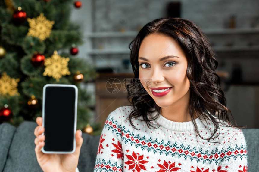 在家中圣诞树附近的沙发上用空白屏幕显示智能手机的图片