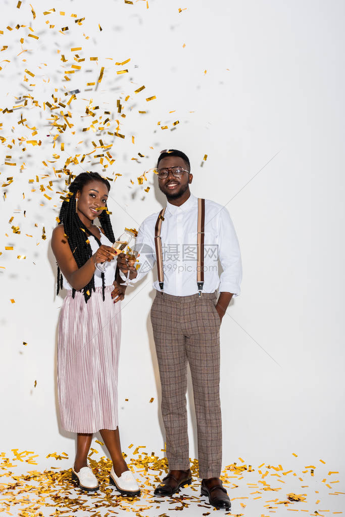 时髦的年轻非裔美夫妇在镜头面前微笑而站在白色和金图片