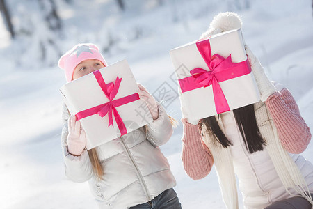 年轻的母亲和她的小女儿在雪地里玩圣诞礼物女孩们在图片