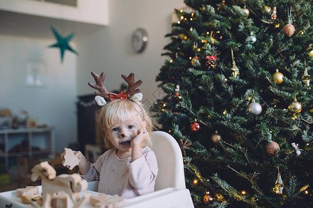 可爱的小女孩穿着有趣的圣诞鹿角和吃饼干图片