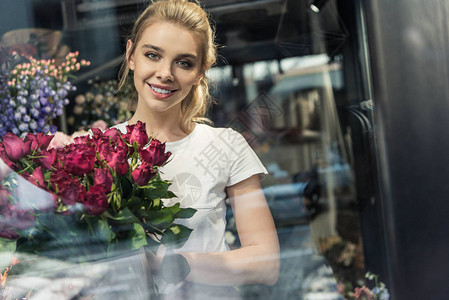 在花店里拿着一束布根底玫瑰花朵的花束以微笑图片