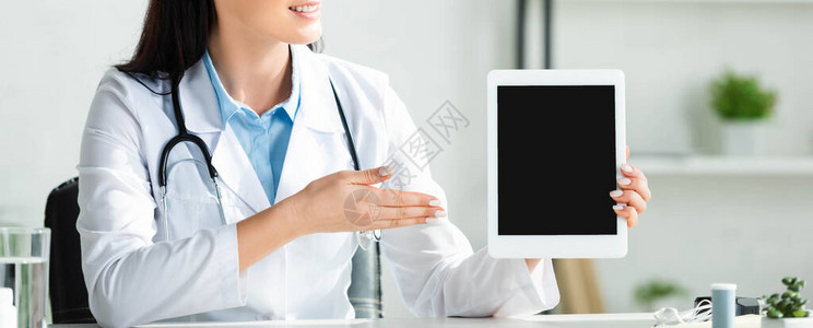 微笑的医生在诊所办公室用空白屏幕展示数字平板图片