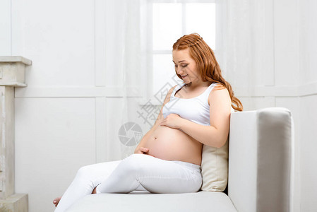 快乐美丽的孕妇坐在家里的沙图片