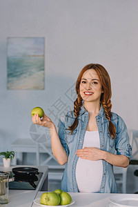 微笑的孕妇在厨房里展示苹果图片
