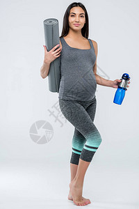 身着运动服的微笑亚洲孕妇拿着瑜伽垫和运动瓶图片