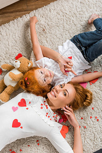 母亲和女儿在地上带着心和泰迪熊躺在图片
