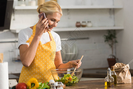 在厨房做饭时用智能手机说话的围裙上笑着微图片