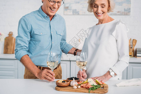 带着酒杯和看家里美味快餐的一对高龄夫妇笑着微图片