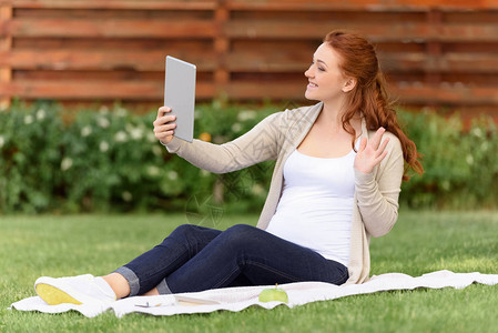坐在绿草坪上用数码平板电脑打视频电话的美丽笑图片