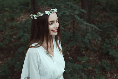 时髦的笑女孩穿着白裙子在树林图片