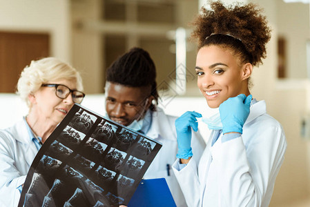 身戴乳胶手套和无菌面罩的非洲青年医生与同事一起笑图片