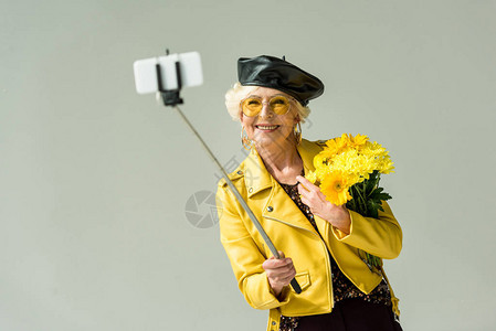 身穿黄色夹克和皮贝雷帽的时尚高级女在智能手机上自拍图片