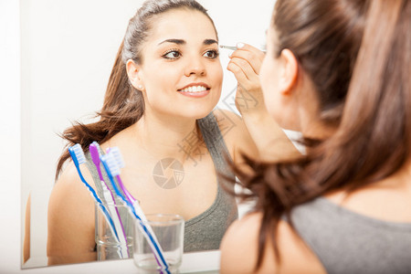 漂亮的年轻女子在浴室的镜子前用镊子拔眉毛图片