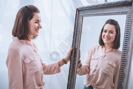 美丽的微笑的年轻女士站在镜子旁边图片