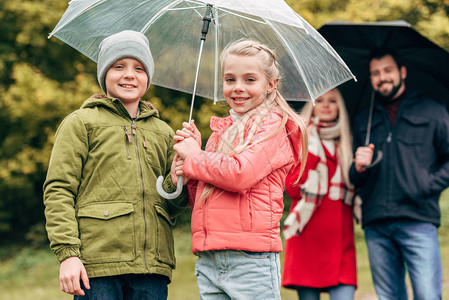 可爱的快乐的孩子和微笑的父母带着雨伞看着秋图片