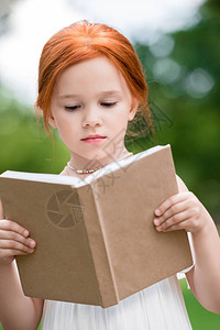 可爱的穿刺红色头发红女孩阅读书公图片