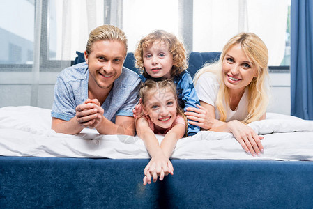 带着两个孩子的年轻快乐家庭与两个孩子一起躺在床上时图片