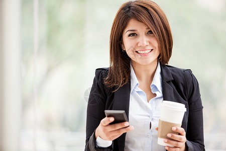 美丽的笑脸女商人在她的手机上发短信并喝咖啡图片