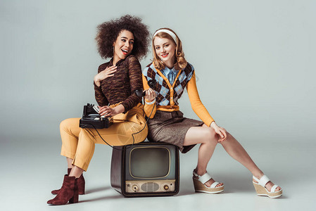 快乐的多元文化复古风格女孩坐在老式电视上图片