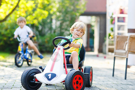 活跃的金发男孩在夏季花园户外驾驶踏板玩具车图片