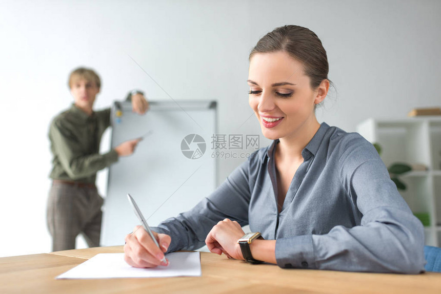 笑的女商人坐在桌子上写下一些东西然图片