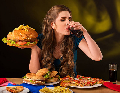 女人吃炸薯条和汉堡包和比萨饼学生在桌子上吃快餐的画像女孩试图在黑暗的背景下吃垃背景图片