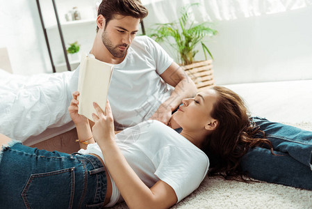 英俊的男人看着女朋友读书躺在卧室地毯图片