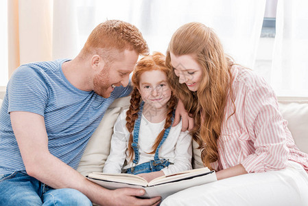 快乐的父母和可爱的小女儿坐在一起看书图片